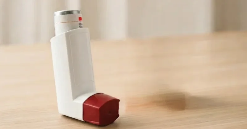 White inhaler with red mouthpiece standing on a wooden table with a softly blurred neutral background