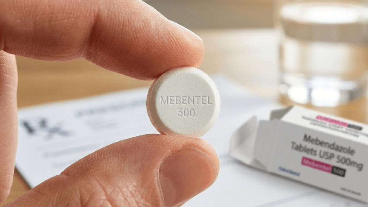 Mebentel 500 mebendazole 500mg chewable tablet held between fingers with product packaging in background